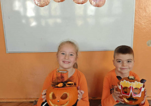 Chłopczyk i dziewczynka siedzą na dywanie obok swoich ozdobionych dyń