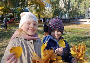 Dwie dziewczynki pokazują swoje bukiety z jesiennych liści