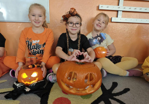 Dzieci siedzące na dywanie ze swoimi ozdobionymi dyniami