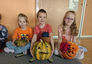 Troje dzieci pokazuje swoje ozdobione dynie
