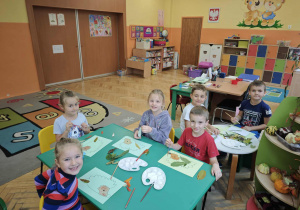 Sześcioro dzieci wykleja liśćmi jeże narysowane na kartkach