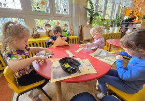 Troje dzieci siedzi przy stoliku i wycina.