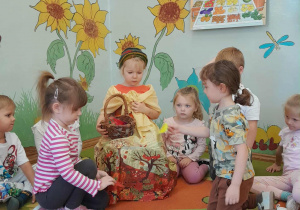 Dzieci siedzą na dywanie, uczestniczą w zabawie "Zbieramy i przeliczamy owoce do kosza Pani Jesieni".