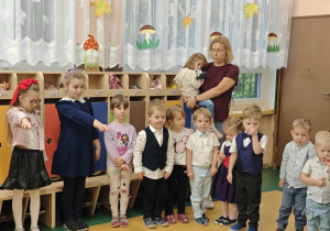 Dzieci stoją przed panią trzymającą na rękach dziecko