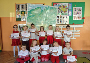 Dzieci z dyplomami w ręku stoją na tle mapy Polski