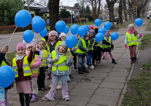 Dzieci spacerują chodnikiem trzymając niebieskie balony