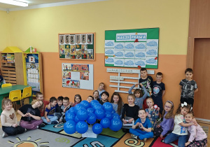 Dzieci siedzą na dywanie obok niebieskich balonów