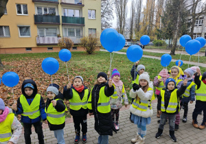 Dzieci ubrane w zielone kamizelki trzymają niebieski balony