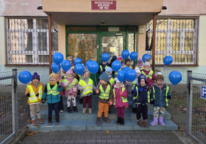 Dzieci stoją na schodach przedszkola z niebieskimi balonami w rękach