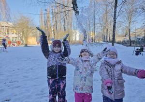 Tzy dziewczynki rzucają śniegiem do góry w ogrodzie przedszkolnym