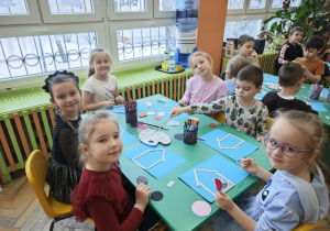 Dzieci wykonują na niebieskie kartce karmniki z drewnianych patyczków