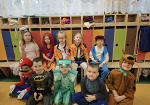 Kilkoro dzieci w strojach karnawałowych siedzą na ławczce