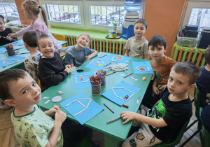 Chłopcy siedzący przy zielonym stole, wykonuja prace plastyczną