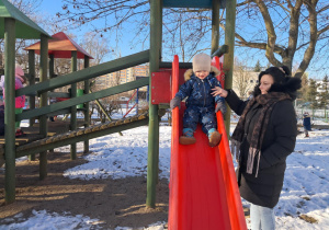 Chłopiec przy pomocy Pani zjeżdża na zjeżdżalni