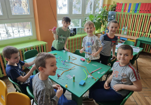 Pięcioro dzieci siedzi przy stoliku na którym są druciki kreatywne i słomki