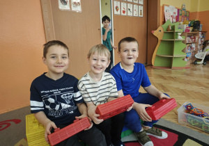 Trzech chłopców trzyma czerwone duże klocki