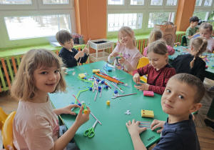 Dzieci siedzą przy stole i tworzą prace z gąbek, drucików kreatywnych i słomek