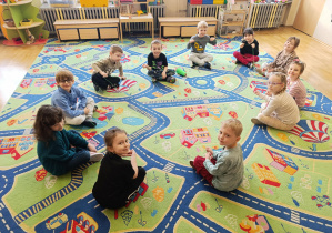 Dzieci siedzą na dywanie trzymając w rękach włóczkę