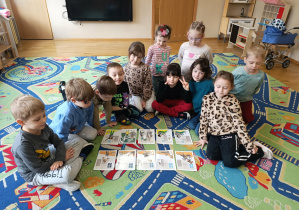 Dzieci siedzą na dywanie i oglądają historyjki obrazkowe dotyczące korzystania z ekranów