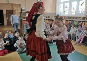 Dziewczynka i pani ubrane w stroje ludowe tańczą