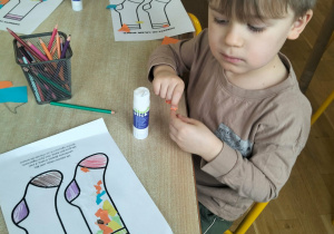 Chłopiec wykleja kontury skarpet kolorowym papierami