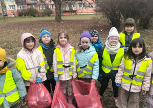 Dzieci ubrane w kamizelki odblaskowe trzymają worki na śmieci