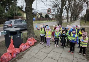 Grupa dzieci stojąca obok kosza na śmieci i różowych worków