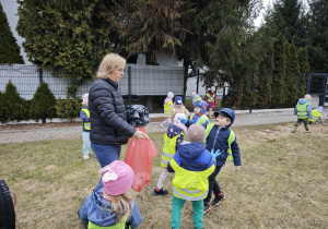 Dzieci wrzucają zebrane śmieci do różowego worka trzymanego przez panią