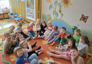 Dzieci siedzące na dywanie z wyciągniętymi nogami do środka koła