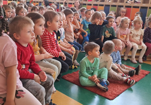 Dzieci siedzące na ławkach i dywaniku