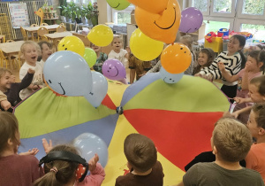 Dzieci trzymając chustę animacyjną w rękach, podrzucają balony do góry