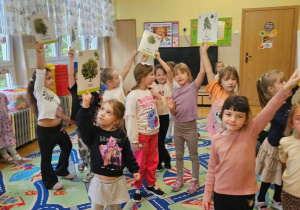 Grupa dzieci unosi ilustracje przedstawiające drzewa