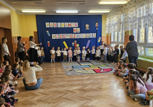 Grupy dzieci w sali w której jest napis pasowanie na przedszkolaka