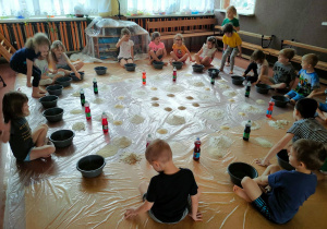 Dzieci mają przed sobą miski, mąkę i zabarwioną wodę.