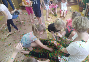 Dzieci obkładają Panią Sylwię kolorowym makaronem