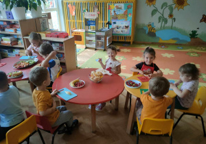 Dzieci siedzą przy stolikach i kroją owoce na sałatkę owocową