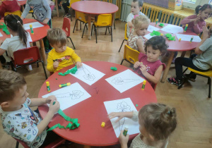 Dzieci siedzą przy stolikach i wykonują z zielonej bibuły kulki do liści marchwi