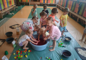Sensoplastyka - dzieci stoją wokół bali z mąką ziemniaczaną oraz barwnikiem spożywczym i wyławiają kolorowe kuleczki