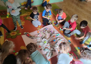 Zabawy ze sztuką - dzieci siedzą na dywanie i doklejają kółeczka do drzewa wykonanego z gazet