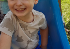 Chłopczyk uśmiecha się do zdjęcia siedząc na zjeżdżalni