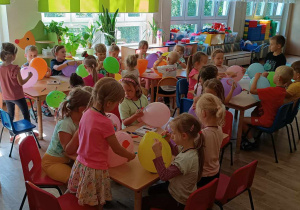 Dzieci siedzą przy stolikach malują balony markerami