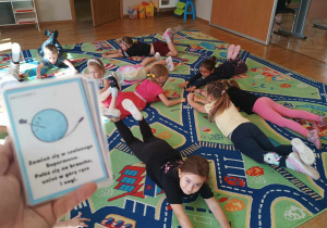 Dzieci wykonują na dywanie ćwiczenie zaproponowane im na kartach obrazkowych