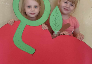 Dwie dziewczynki uśmiechają się trzymając wielkie jabłko wycięte z papieru