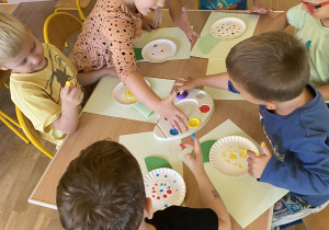 Dzieci malują paluszkami na papierowych talerzykach