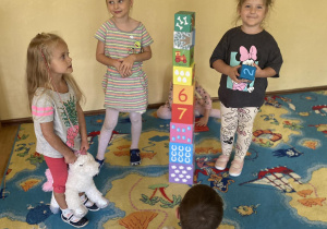 czworo dzieci buduje z klocków na niebieskim dywanie