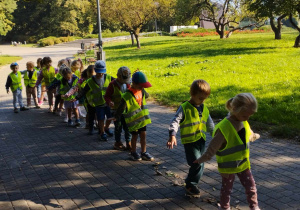 Jesień w parku - dzieci przechodzą jedno za drugim po ścieżce ułożonej z liści