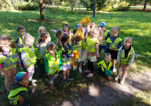 Jesień w parku - dzieci stoją jedno obok drugiego i pokazują worek z kasztanami, które pozbierały w parku