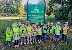 Jesień w parku - dzieci stoją przed tablicą z nazwą parku, który odwiedziły