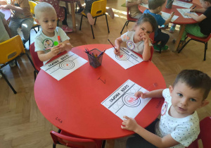 Dzień kropki - troje dzieci siedzi przy stoliku i koloruje opaski na głowę