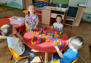 Czworo dzieci siedzi przy stoliku i bawi się klockami